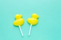 Bright yellow duck shaped candies on sticks on light green background. Royalty Free Stock Photo
