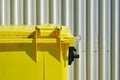 Bright yellow dumpster against a white industrial corrugated cladding or wall siding