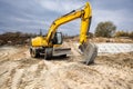 Bright yellow excavator digs into the earth at a construction site surrounded by trees, showcasing the hard work involved in Royalty Free Stock Photo