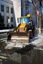 Bright yellow excavator tractor cleaning snow on the road along houses, front view, snowy winter in Kharkiv