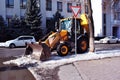 Bright yellow excavator tractor cleaning snow on the road along street, side view, snowy winter in Kharkiv