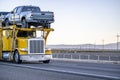 Bright yellow industrial standard big rig car hauler semi truck transporting pick up trucks on two level modular semi trailer