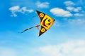 Bright yellow kite with smiles flying in the blue sky on a sunny day Royalty Free Stock Photo
