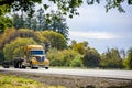 Big rig yellow bonnet semi truck with chrome grille and exhaust pipes transporting step down semi trailer running on the autumn Royalty Free Stock Photo