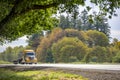 Yellow big rig bonnet semi truck with step down semi trailer running on the green highway road Royalty Free Stock Photo