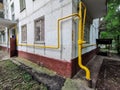 Bright yellow metal pipe of household gas along an old residential high-rise building