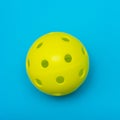 Bright yellow pickleball or whiffle ball on a solid aqua blue flat lay background symbolizing sports and activity with copy space