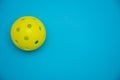 Bright yellow pickleball or whiffle ball on a solid bright blue flat lay background symbolizing sports and activity with copy