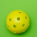 Bright yellow pickleball or whiffle ball on a solid bright green flat lay background symbolizing sports and activity with copy
