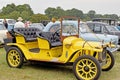 A bright yellow retro car on show with people looking round the other cars on show.