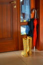 Bright yellow rubber boots with red and black umbrellas by wood door with stained glass windows in stylish interior. Home entrance
