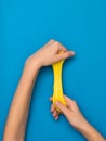 Bright yellow slime stretched out in the hands on a bright blue background.