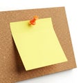 Bright yellow sticky note pinned to a corkboard with an orange pushpin Royalty Free Stock Photo