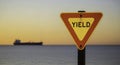 Bright yellow triangular YIELD sign on pole against calm ocean and sunset sky with ship Royalty Free Stock Photo