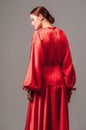 Bright young lady in red dress with long wide sleeves and sexy neckline on high heels mooving on grey studio background