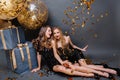 Brightful happy moments at celebrating party of two amazing young women in luxury black dresses chilling on floor on Royalty Free Stock Photo