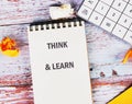 Brightly arranged on a wooden surface, a notebook displays THINK and LEARN, accompanied by a calculator and crumpled