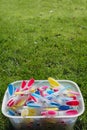 Brightly coloured clothes pegs in a bucket on green grass in sun Royalty Free Stock Photo