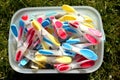 Brightly coloured clothes pegs in a bucket on green grass in sun Royalty Free Stock Photo