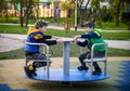 Brightly dressed twin brothers play on a carousel in an autumn park amid fallen yellow leaves. They are two years old Royalty Free Stock Photo