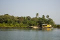 A brightly green jungle with palm trees and a yellow house with a boat against the backdrop of the sea coast and a clean blue sky Royalty Free Stock Photo