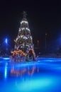 Brightly illuminated ice rink with Christmas tree with decorations on the center