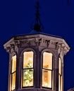 Brightly lit Christmas tree beams brightly from a cupola atop a white New Eland style house