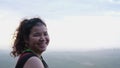 Brightly lit portrait of cheerful girl on top of mountain with beautiful view background in early morning