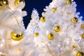 Brightly lit white artificial Christmas trees at night. Golden balls covered with drops of water, and garlands hanging on white Royalty Free Stock Photo