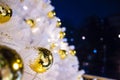 Brightly lit white artificial Christmas trees at night. Golden balls covered with drops of water, and garlands hanging on white Royalty Free Stock Photo