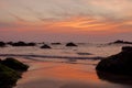 A Brightly orange blue gray purple cloud lines in the sunset sky over the sea with rocks and a sandy beach Royalty Free Stock Photo