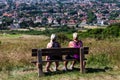 Brighton, UK - June 2018 Two Women Hikers Resting on Wooden Bench on Higher Ground. Houses and Trees Overcrowding at the