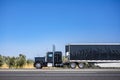 Brilliant black big rig classic semi truck tractor transporting cargo in covered reefer semi trailer driving on the flat Royalty Free Stock Photo