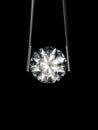 Brilliant cut diamond held by tweezers on a black background. Beautiful sparkling shining round shape.