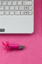 Brilliant pink usb flash memory card with a pink bow lies on a blanket of soft and furry light pink fleece fabric beside to a whi