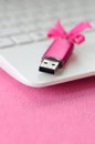 Brilliant pink usb flash memory card with a pink bow lies on a blanket of soft and furry light pink fleece fabric beside to a whi