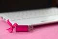 Brilliant pink usb flash memory card with a pink bow lies on a blanket of soft and furry light pink fleece fabric beside to a whi