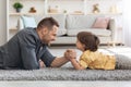 Bringing up strong kid. Happy father competing arm wrestling match with his little boy, lying together on floor at home Royalty Free Stock Photo