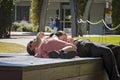 A man and woman rest in the sun on a wooden bench in the city