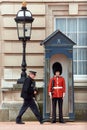 British policeman walking past a royal guard at the entrance to his sentry box at Buckingham Palace