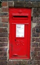 British Royal Mail red post box set in a brick wall