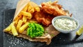 British Traditional Fish and chips with mashed peas, tartar sauce on crumpled paper.