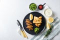 British Traditional Fish and chips with minty mashed peas detail and a slice of lemon. on black round plate over white lintn and