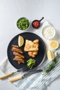 British Traditional Fish and chips with minty mashed peas detail and a slice of lemon. on black round plate over white lintn and