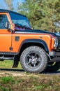 An orange Land Rover Defender parked on the road in autumn