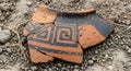 Broken ancient ceramic vase shards found in excavation site. Old earthenware fragment with geometric black decorations lying on Royalty Free Stock Photo