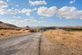 Broken asphalt road in the dry grass valley of the Middle East under white clouds