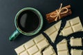 Broken bar of white chocolate, cinnamon and cup of coffee an black table, top view Royalty Free Stock Photo