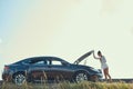 Broken black car standing near field with woman checking its Royalty Free Stock Photo