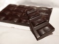 Broken black chocolate bar on white wrapping paper Royalty Free Stock Photo